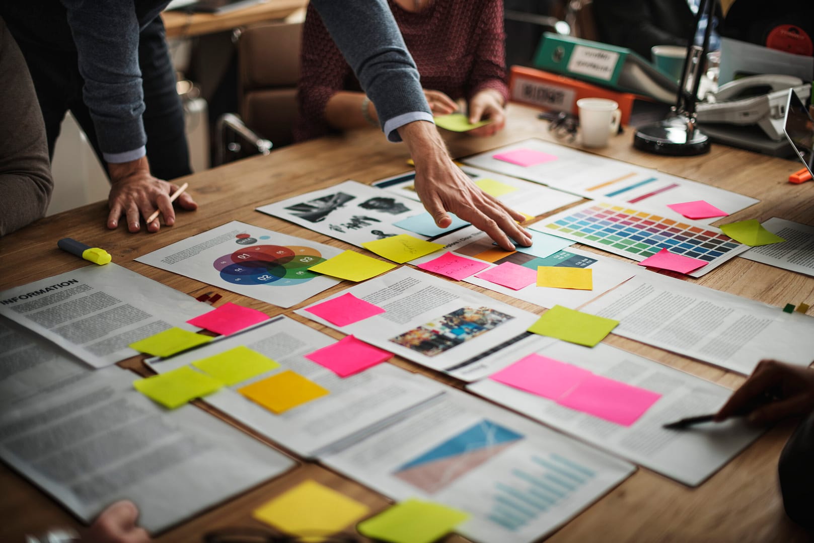 A team collaborating on a project management strategy, reviewing documents, color-coded sticky notes, and charts to organize tasks and workflows