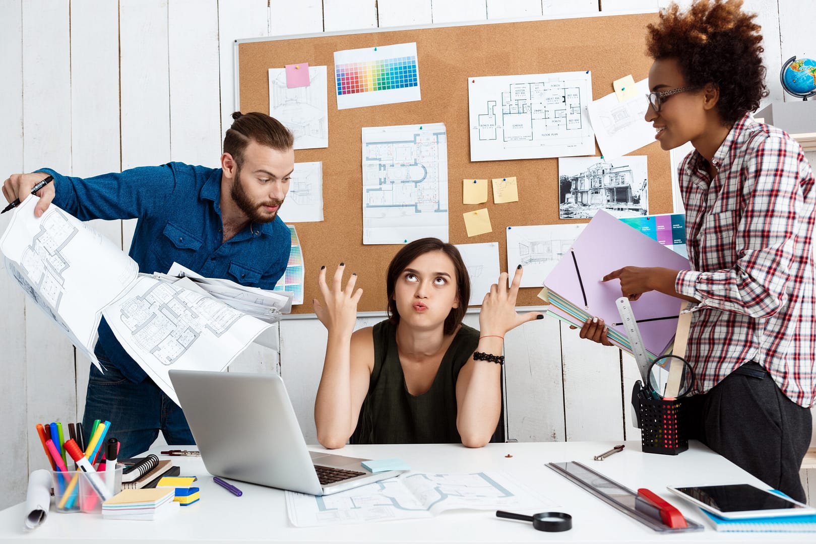 Three colleagues in a tense discussion over project plans, with one person looking frustrated.